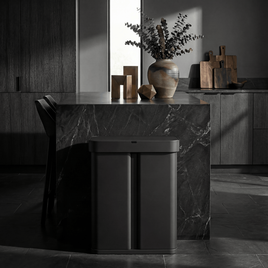 Simplehuman's 58L Sensor Can in Matte Black in a darker background with black countertop and cabinets featuring warm, wooden trinkets on the countertop and cutting boards in the background.