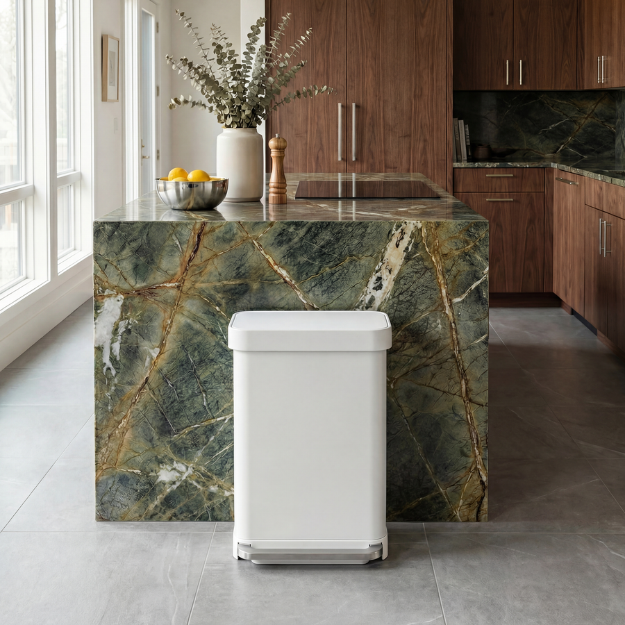 Simplehuman's 55L Step Can in white in a bright and airy kitchen setting with jade colored countertops, wood cabinetry, and white walls with floor to ceiling windows.